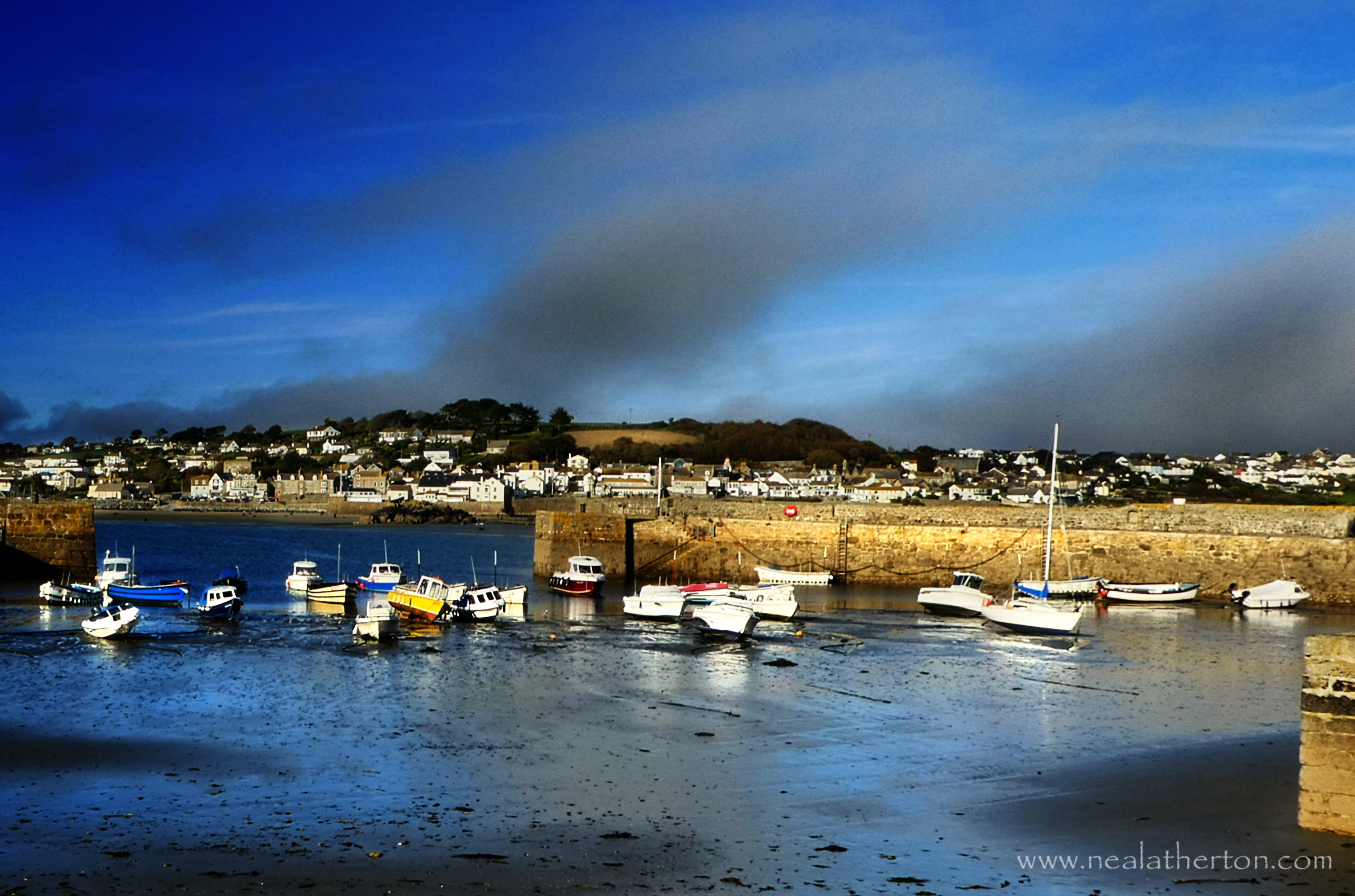 boats in harbour with stone jetty with town beyond the sea and stormy sky