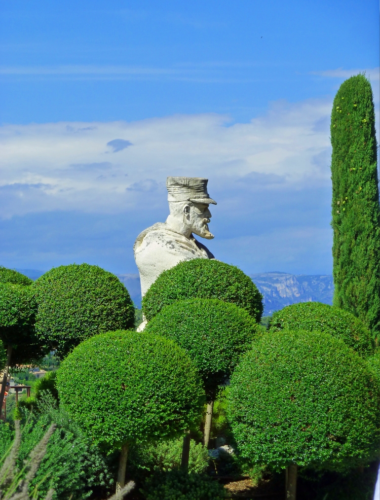 statue of military man in Provence behind topiary bushes and mountains with blue sky