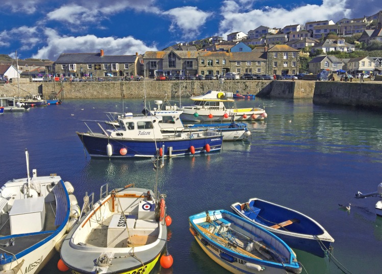 several boats moored in harbour with quat=yside with pub and shops with houses on hillside
