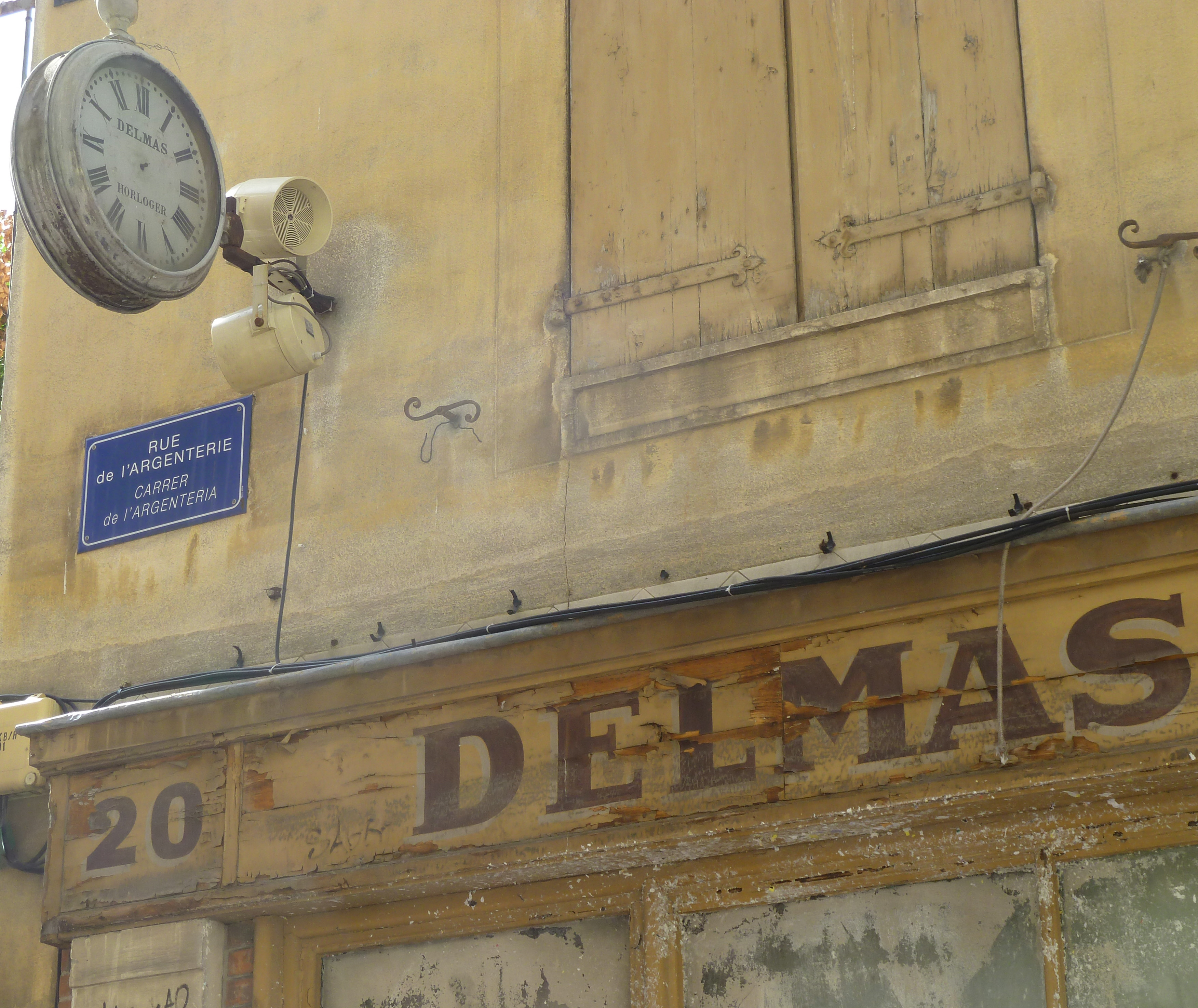 old shop front with lettering and street sign with clock and wooden shutters
