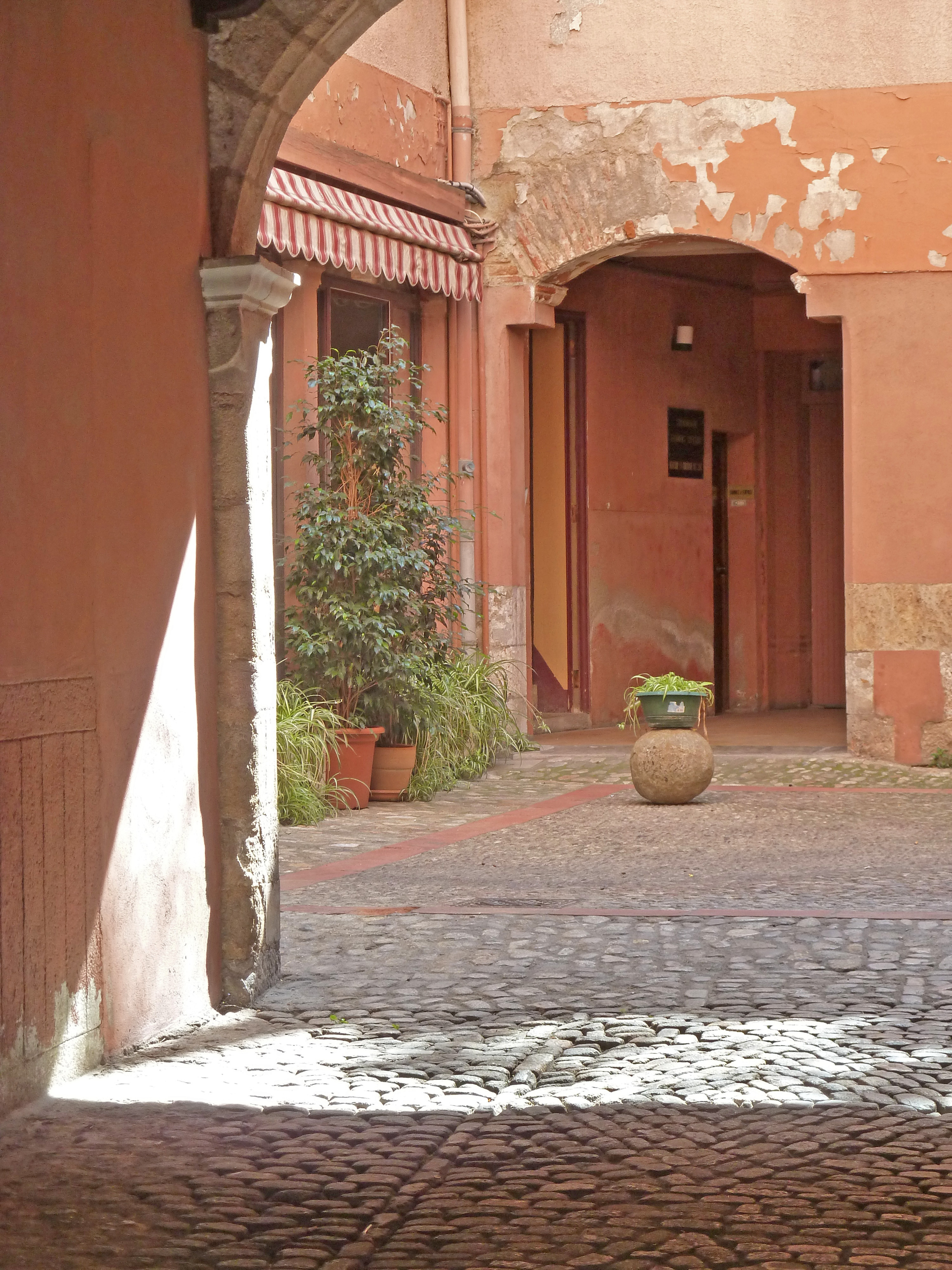 cobbled courtyard with sun shining and stone archway with plants