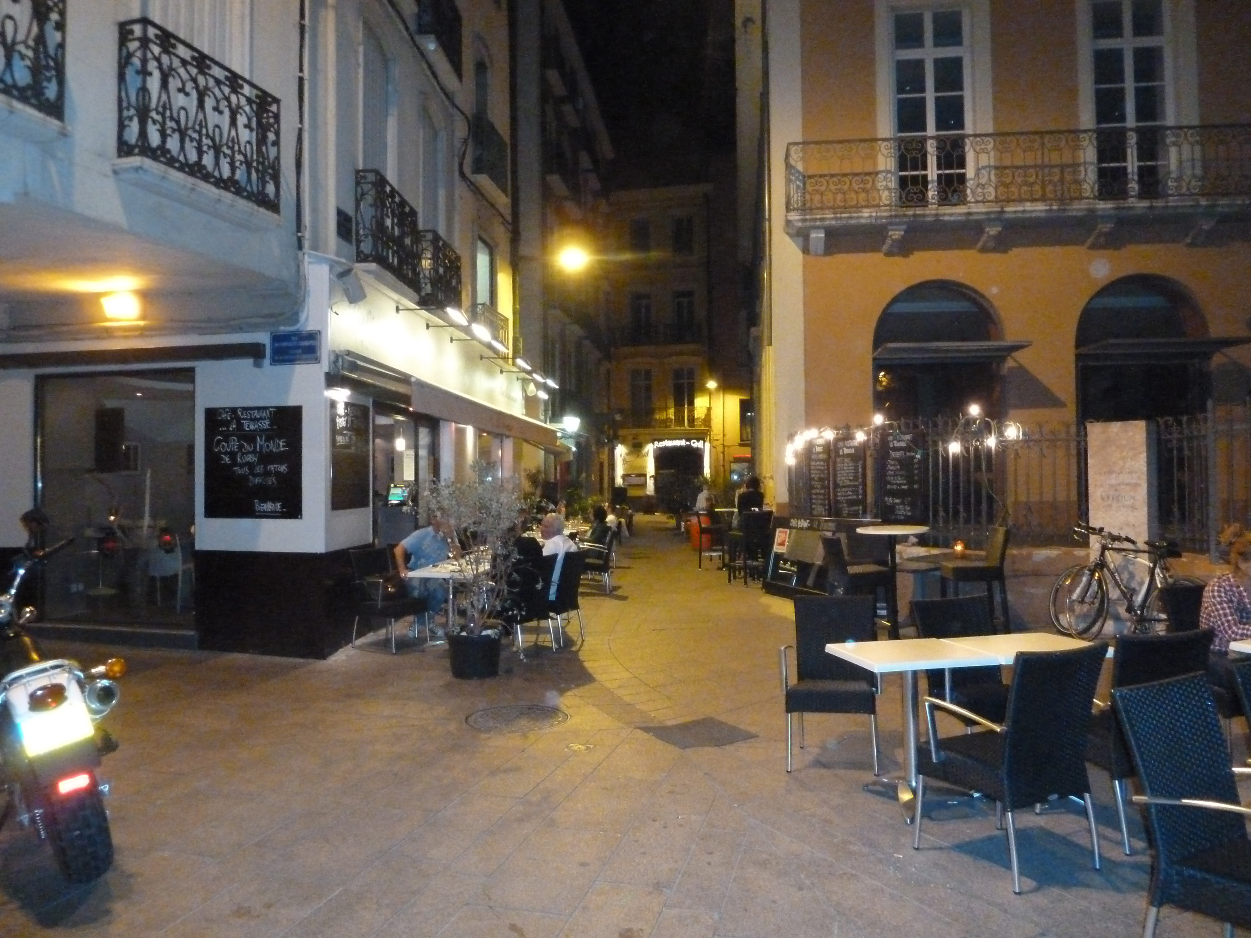 Night in street with restaurants and tables with men drinling and motorcycle