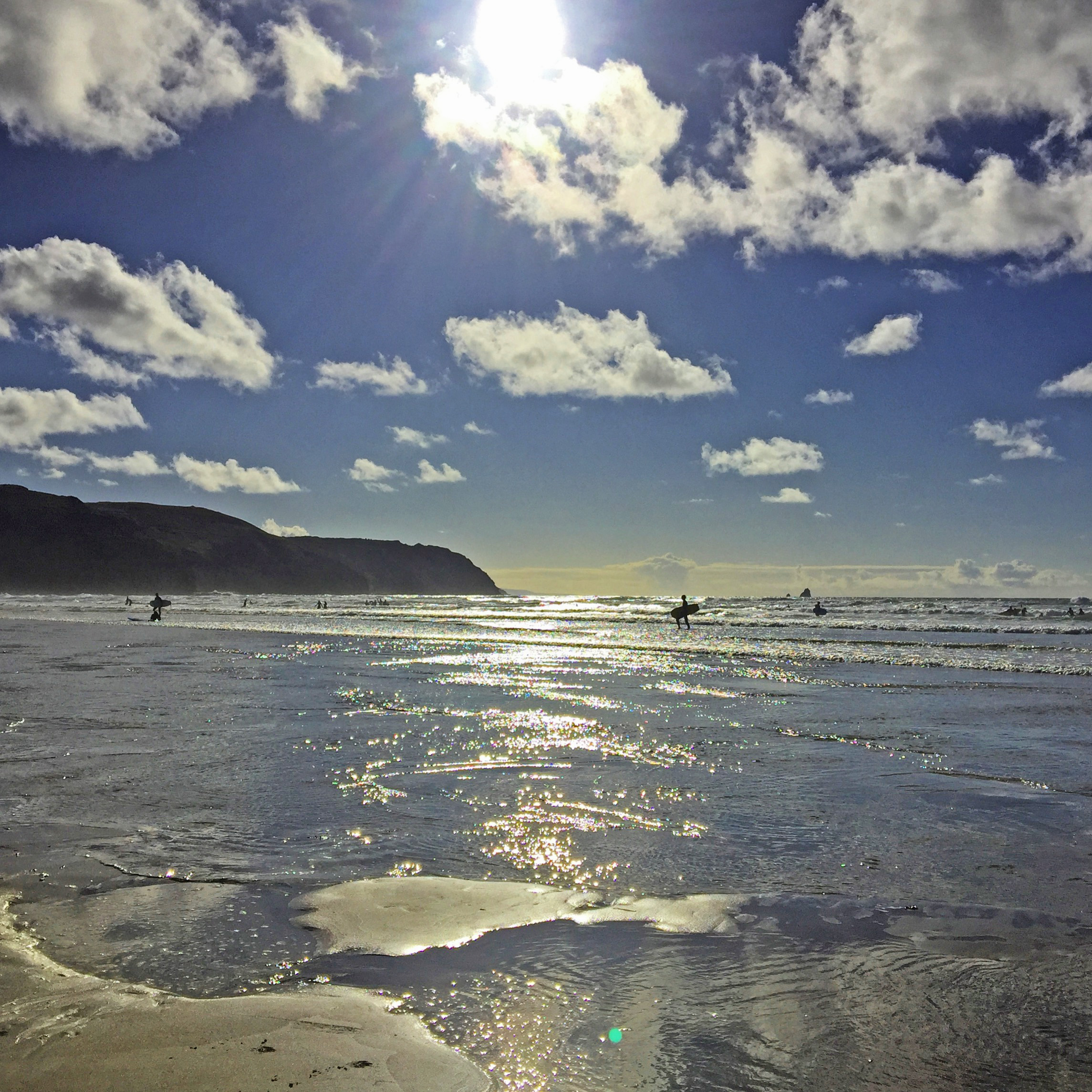 incoming tide with surfers on waves and cliffs under blue sky with clouds