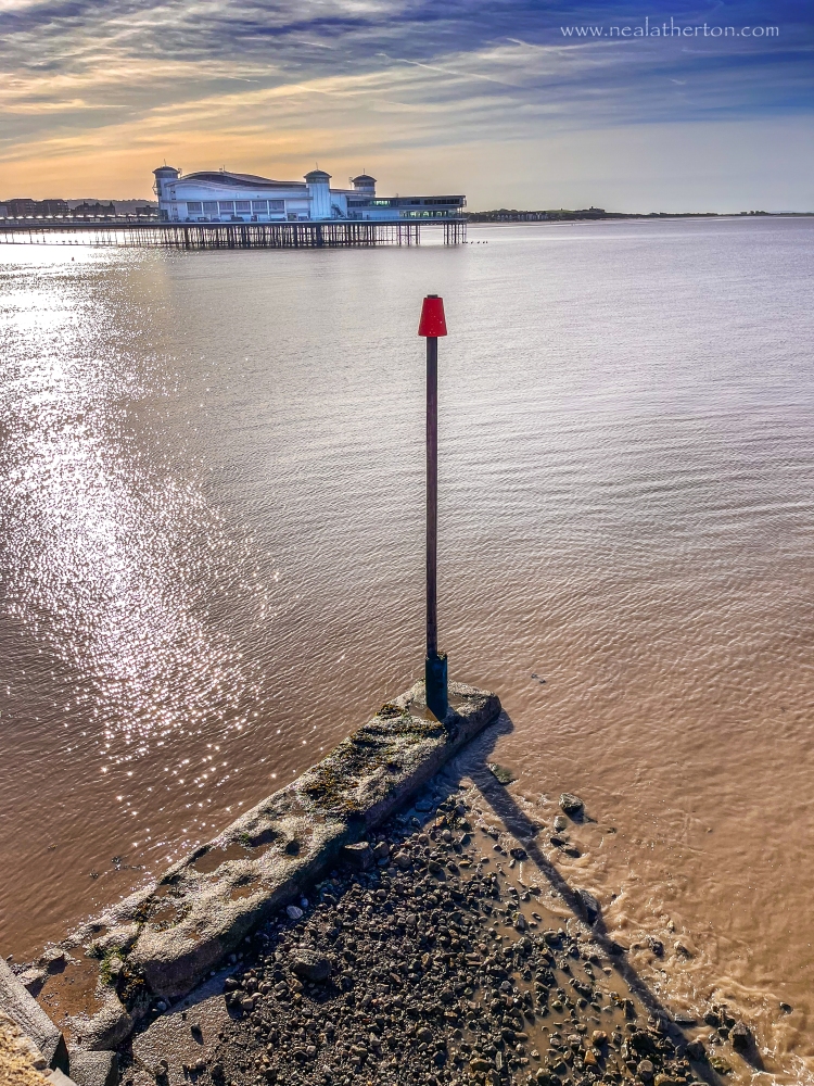 Pole on concrete base in the sea with pier and early morning sky
