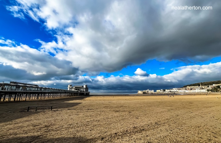 Quiet Weston Super Mare beach between the pier and buildings on the island with dark stormy clouds above