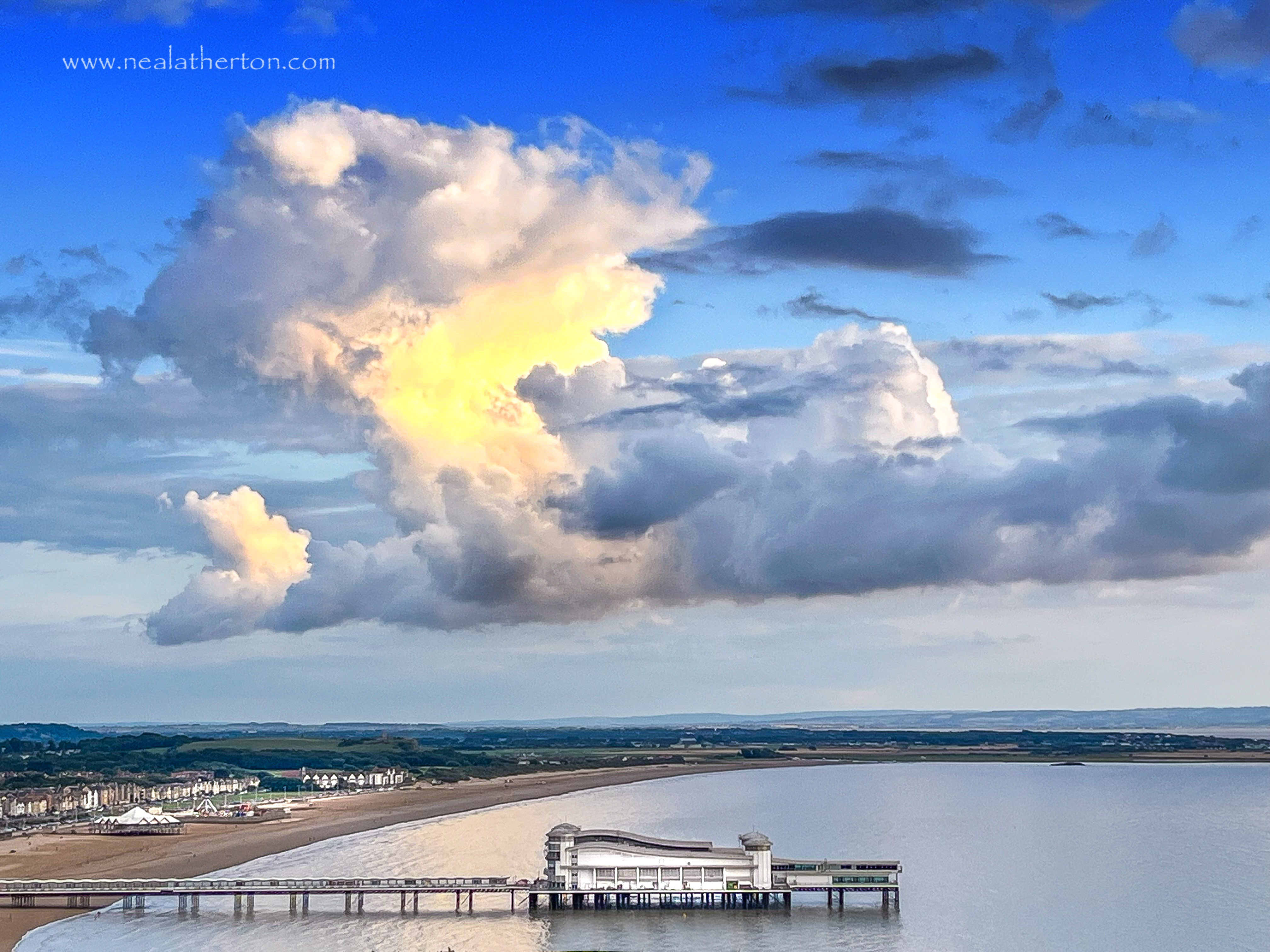 Pier sat in water in bay with striking clouds against a ble winter sky over a beach