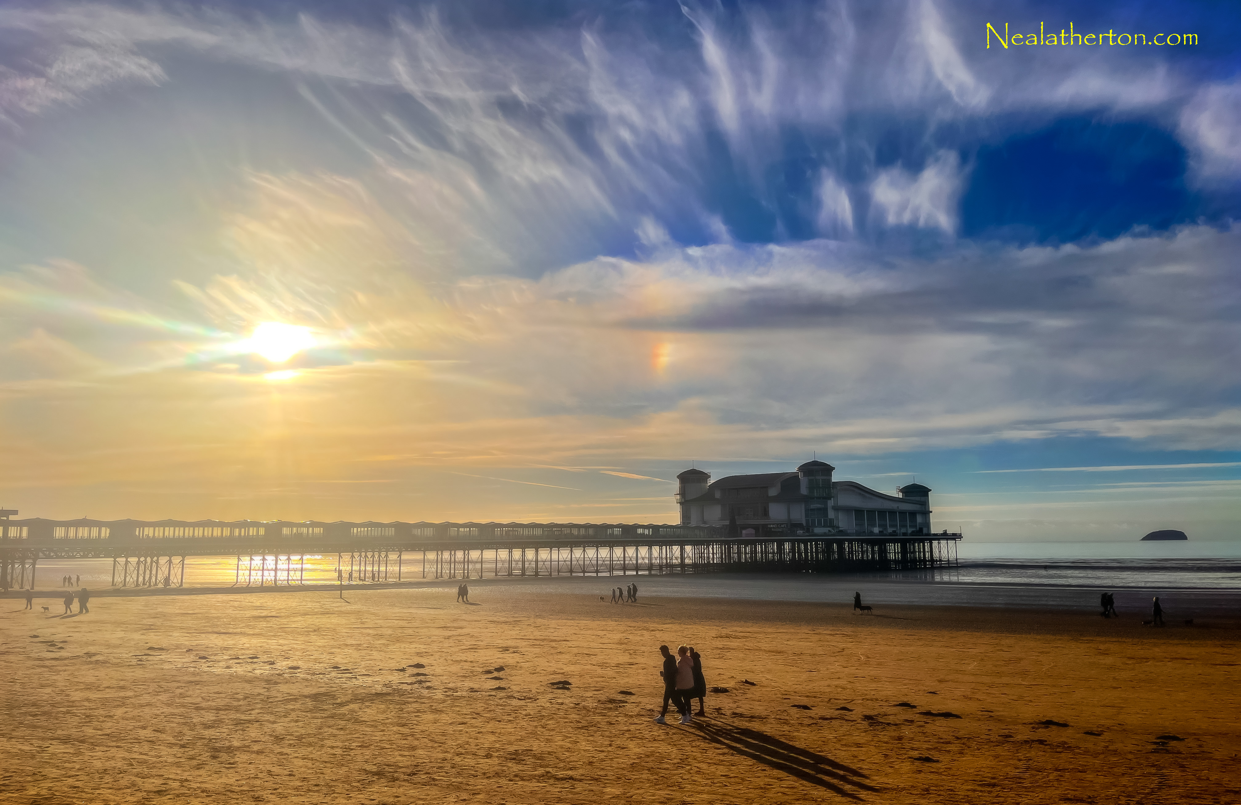 three people walking on beach in front of pier with sea and wintery sky