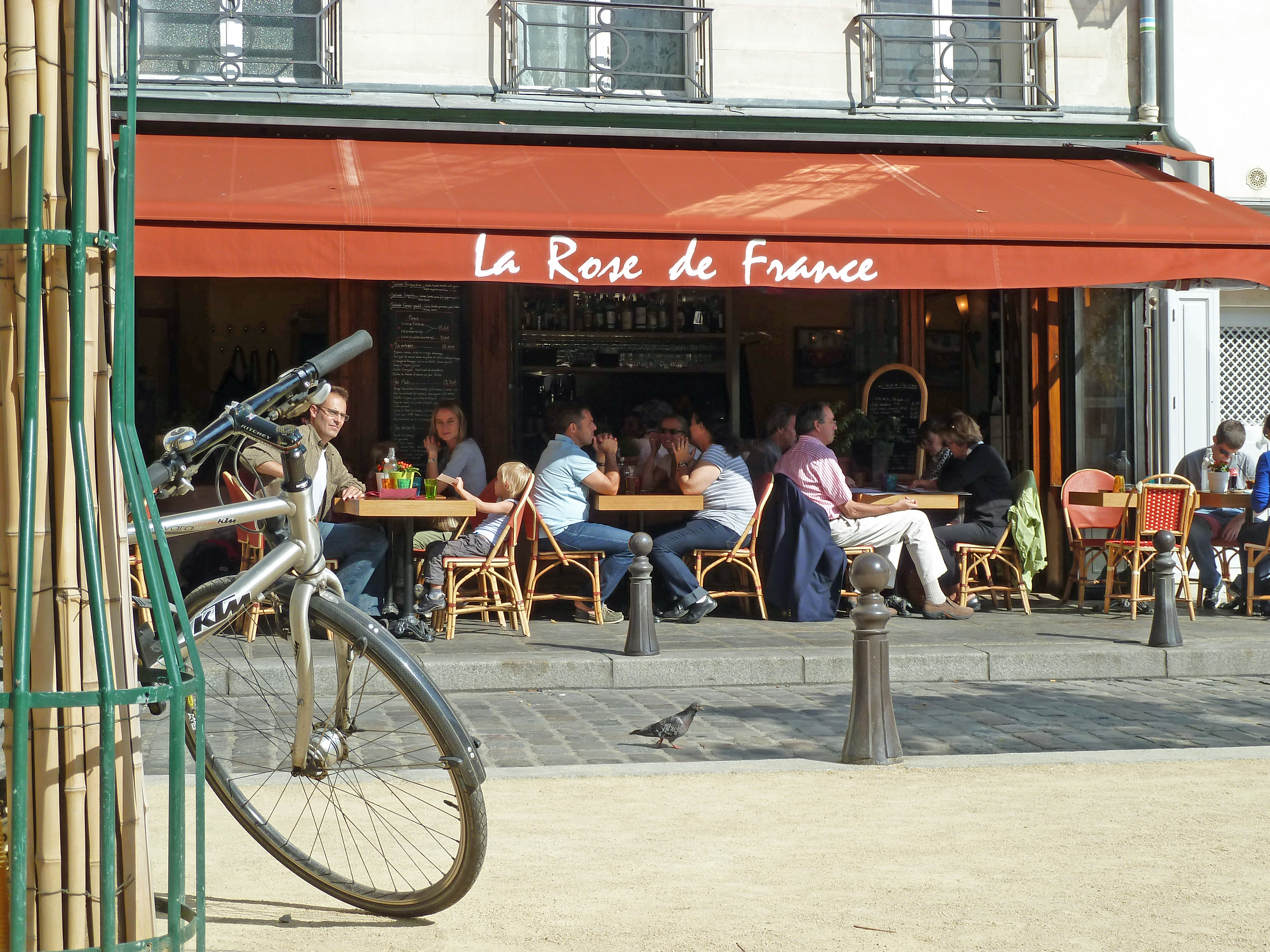 cycle by post on gravel near cobbled street with restaurant terrace