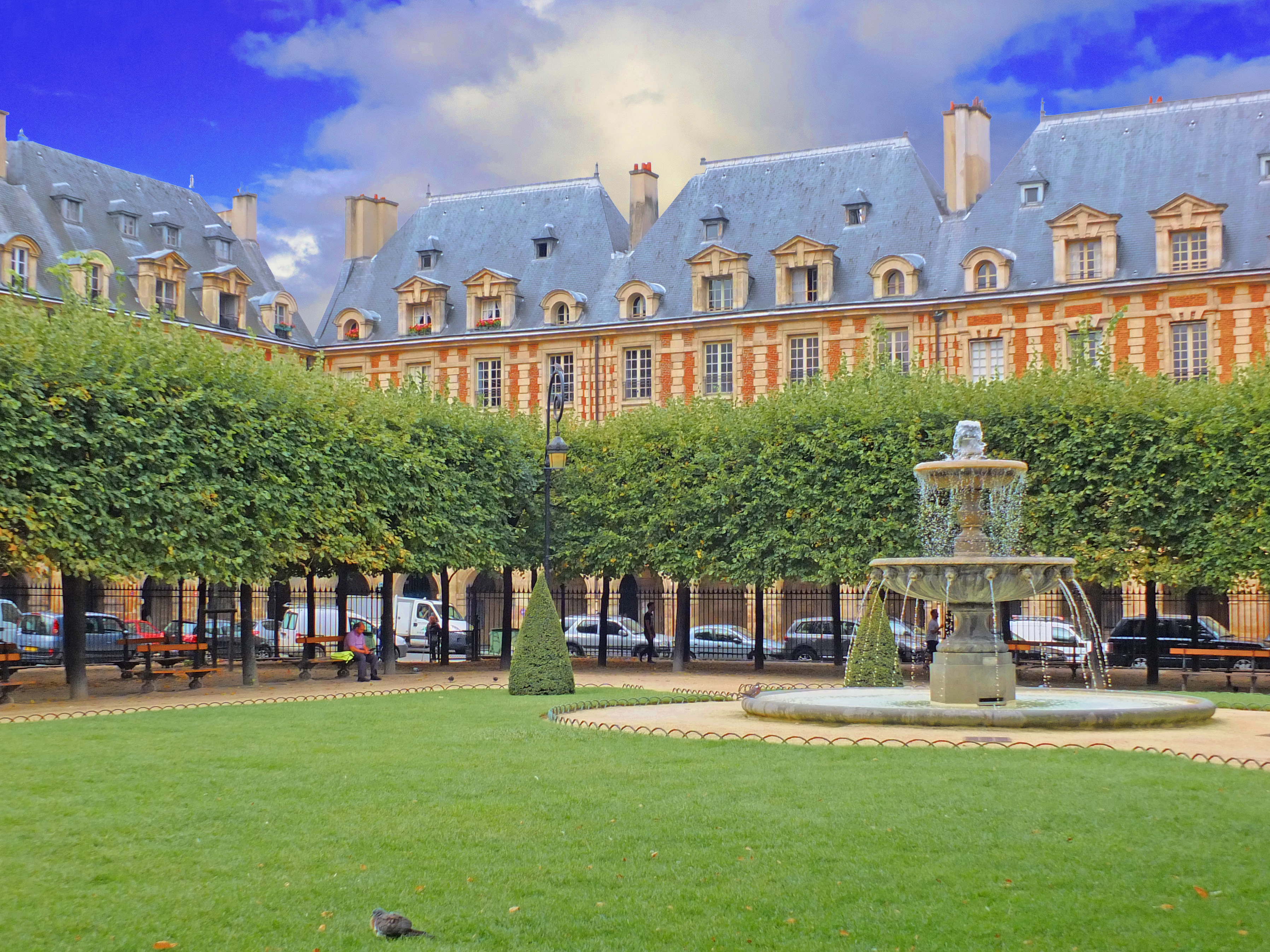 fountain with grass around and trees with architece from 16th century around a square
