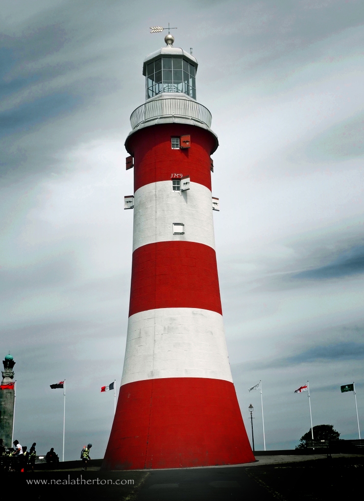 red and white hooped lighthouse with flags and grey sky