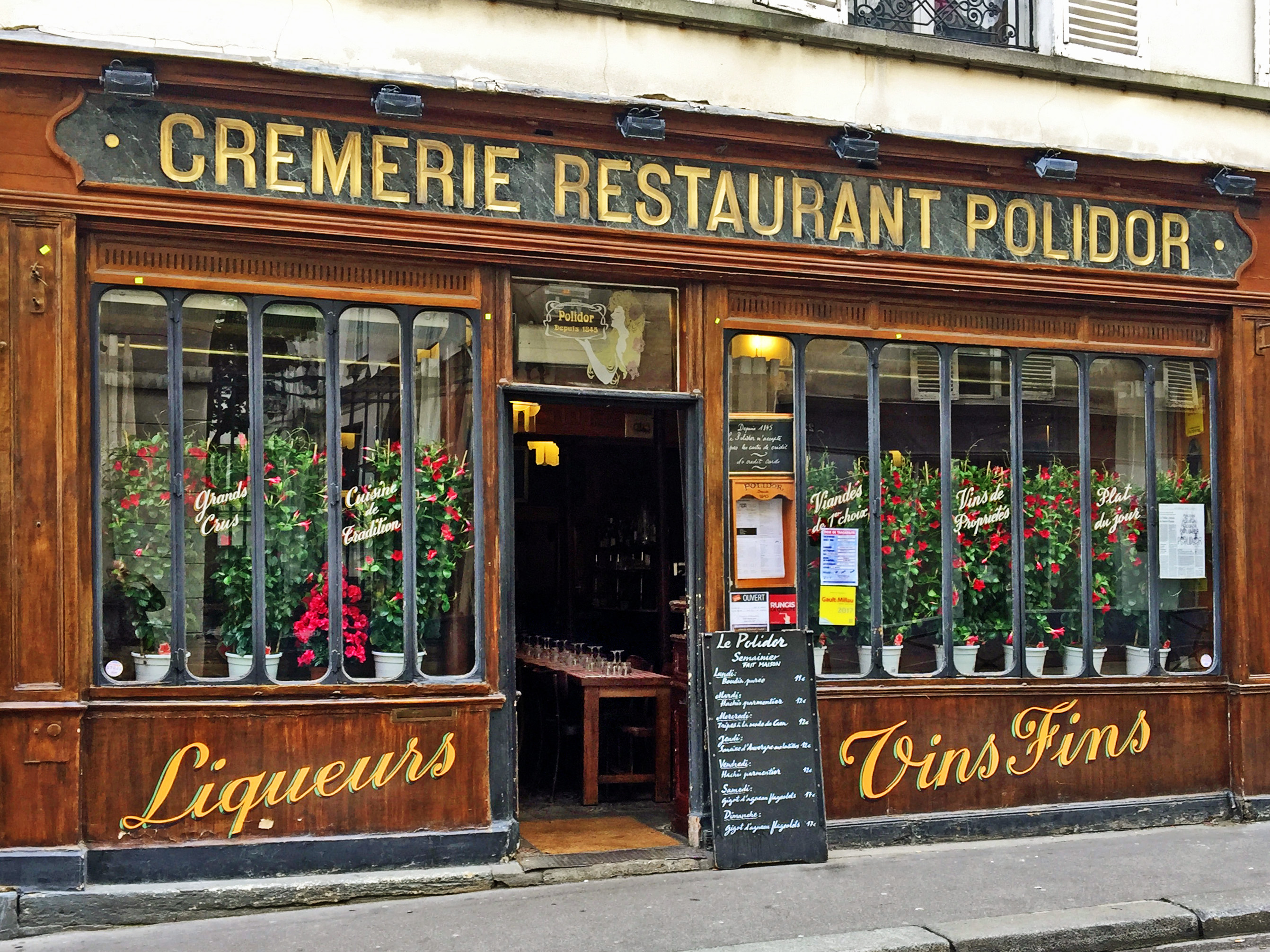 old wooden frontage to restaurant with gold lettering and plants in window and menu board