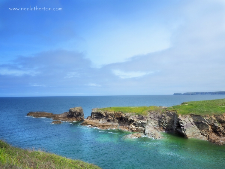 headland with small cliffs and grassy top with harbour inlet blue sea and sky
