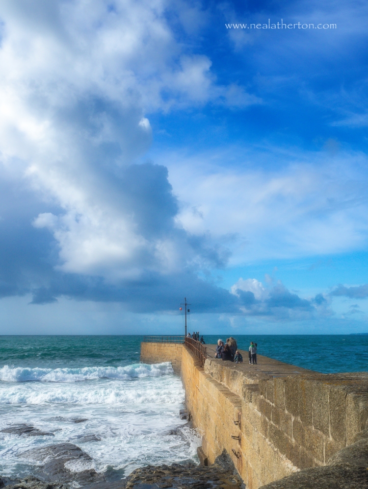 stone pier at harbour entrance with lively sea and waves and stormy sky