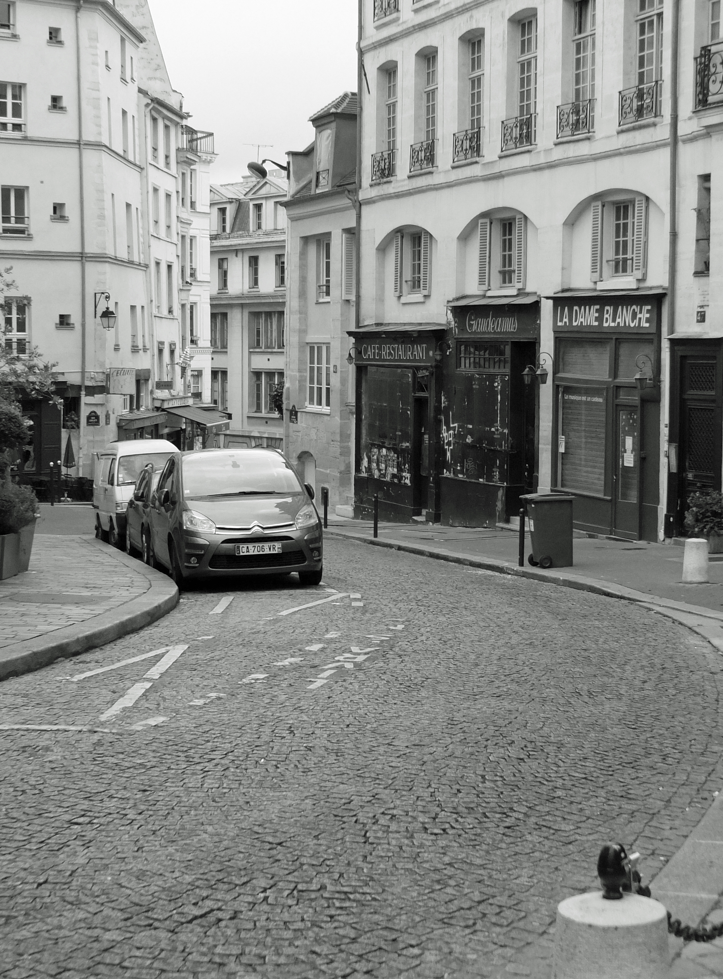 cars parked on cobbled steet with buildings and shops