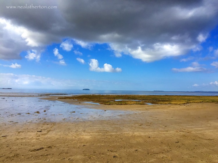 beach with incoming sea and islands in distance under threatening sky