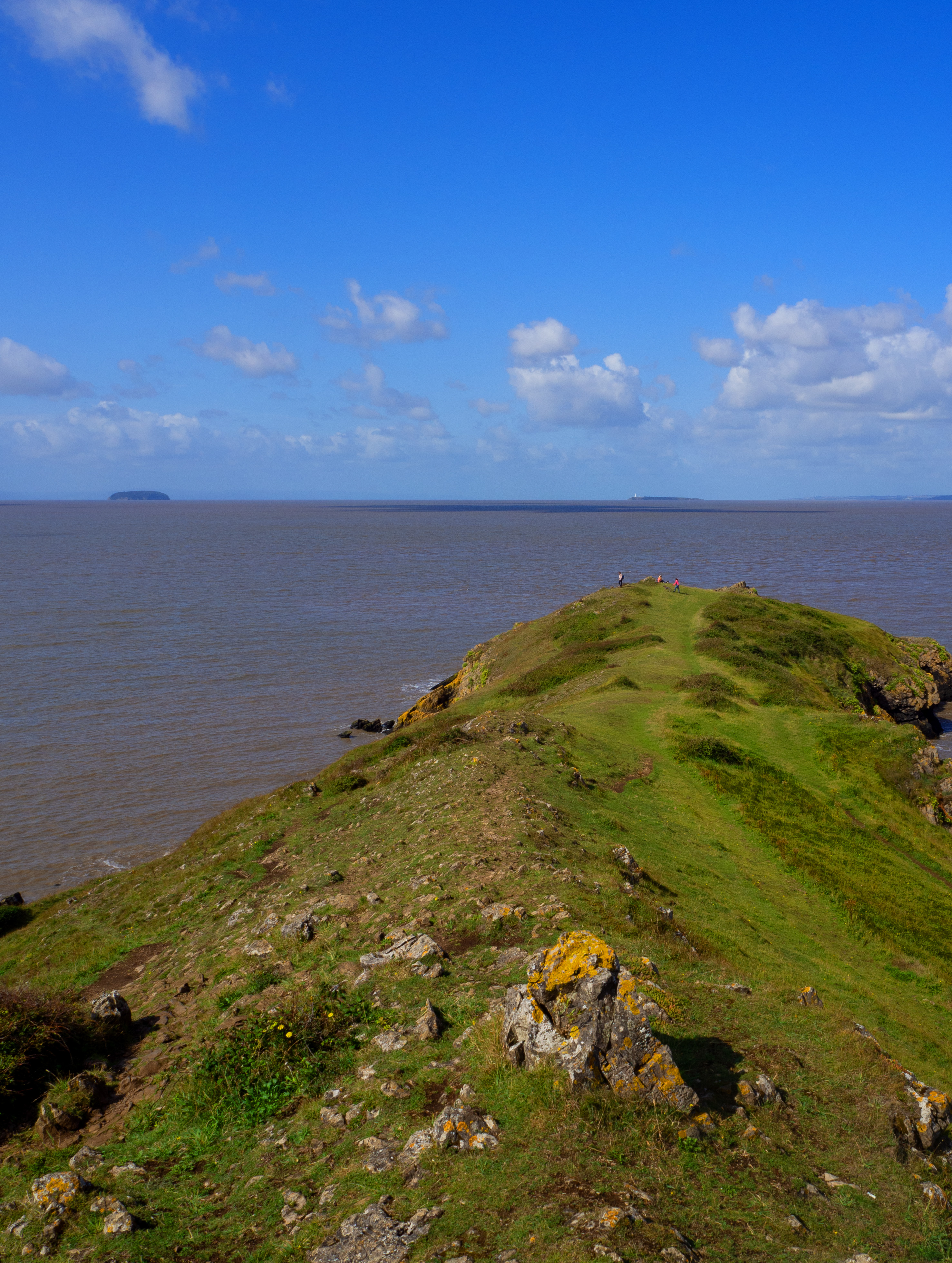 end of land with grass and rocks with sea and islands