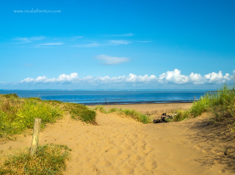 Sandy path betwen dunes with wooden post and beach and sea with blue summer sky