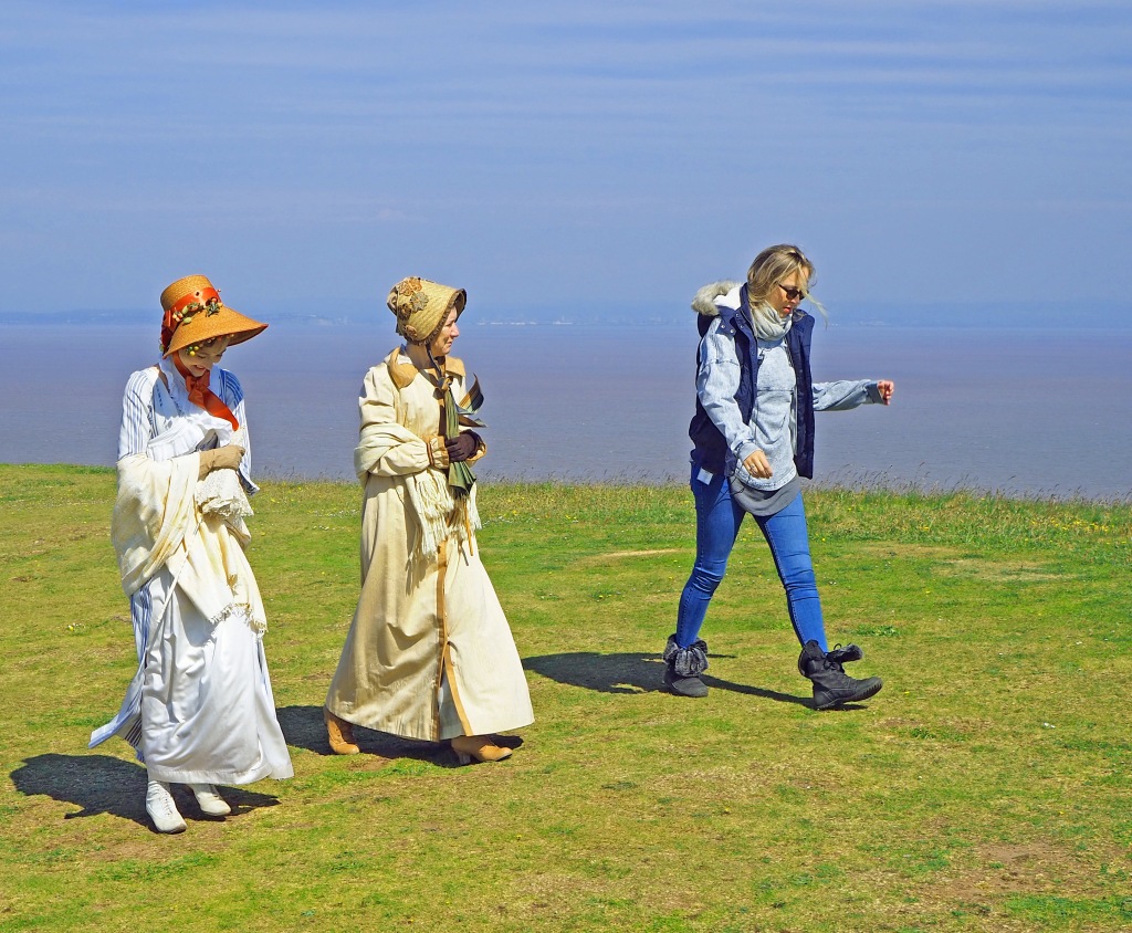 Two actors and director on grassy bank filming period drama in costume