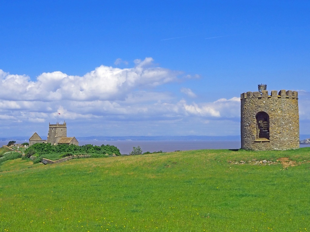 stone tower and beacon on grassy hill with church and sea