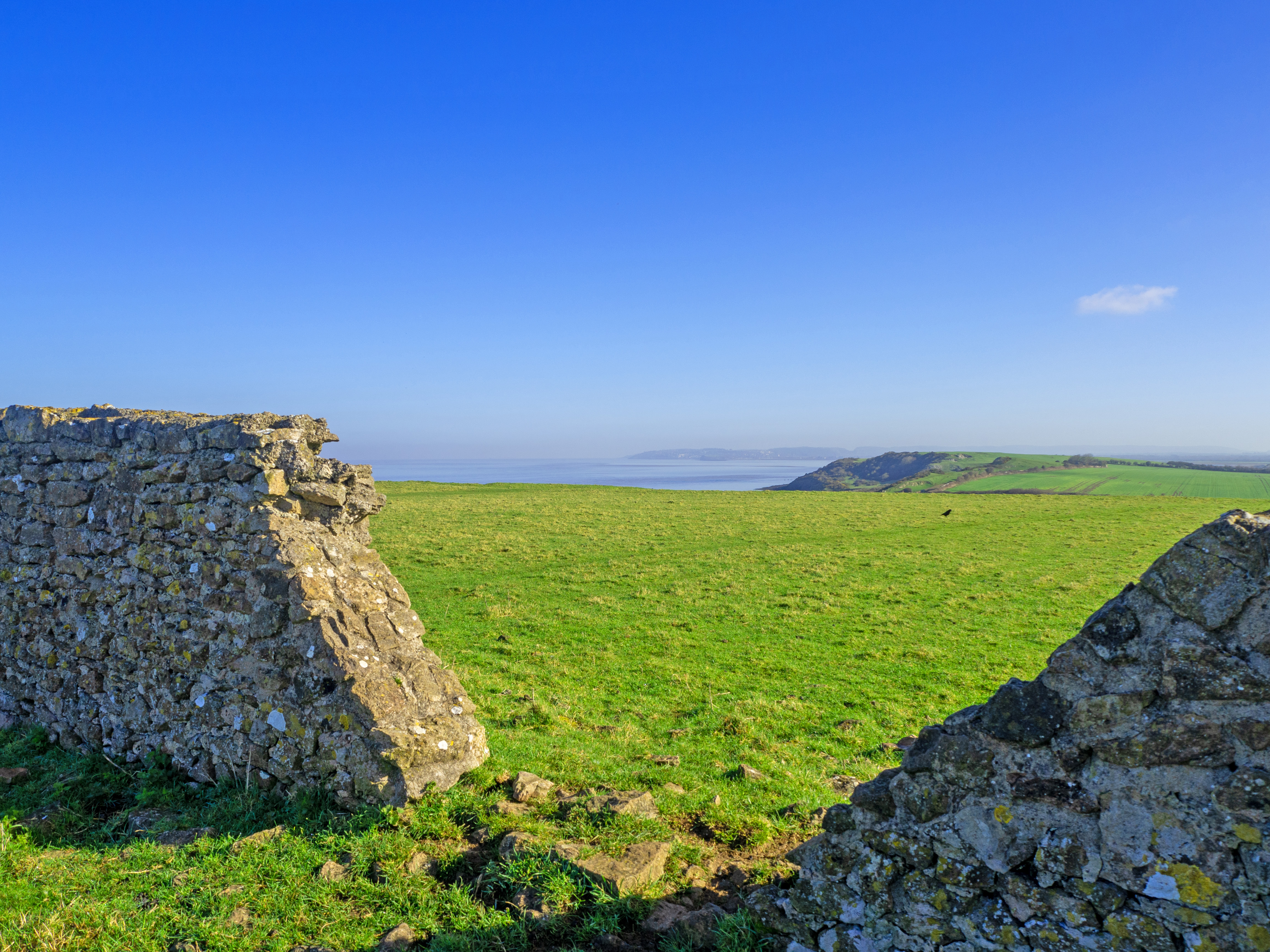 stone broken wall with grassy fields bith blue sky and sea