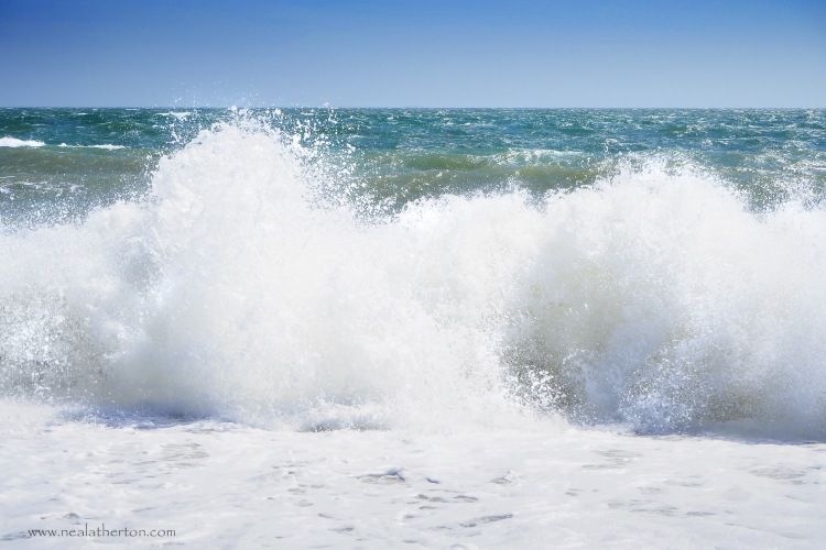 waves crash onto beach with heavy blue sea and sky