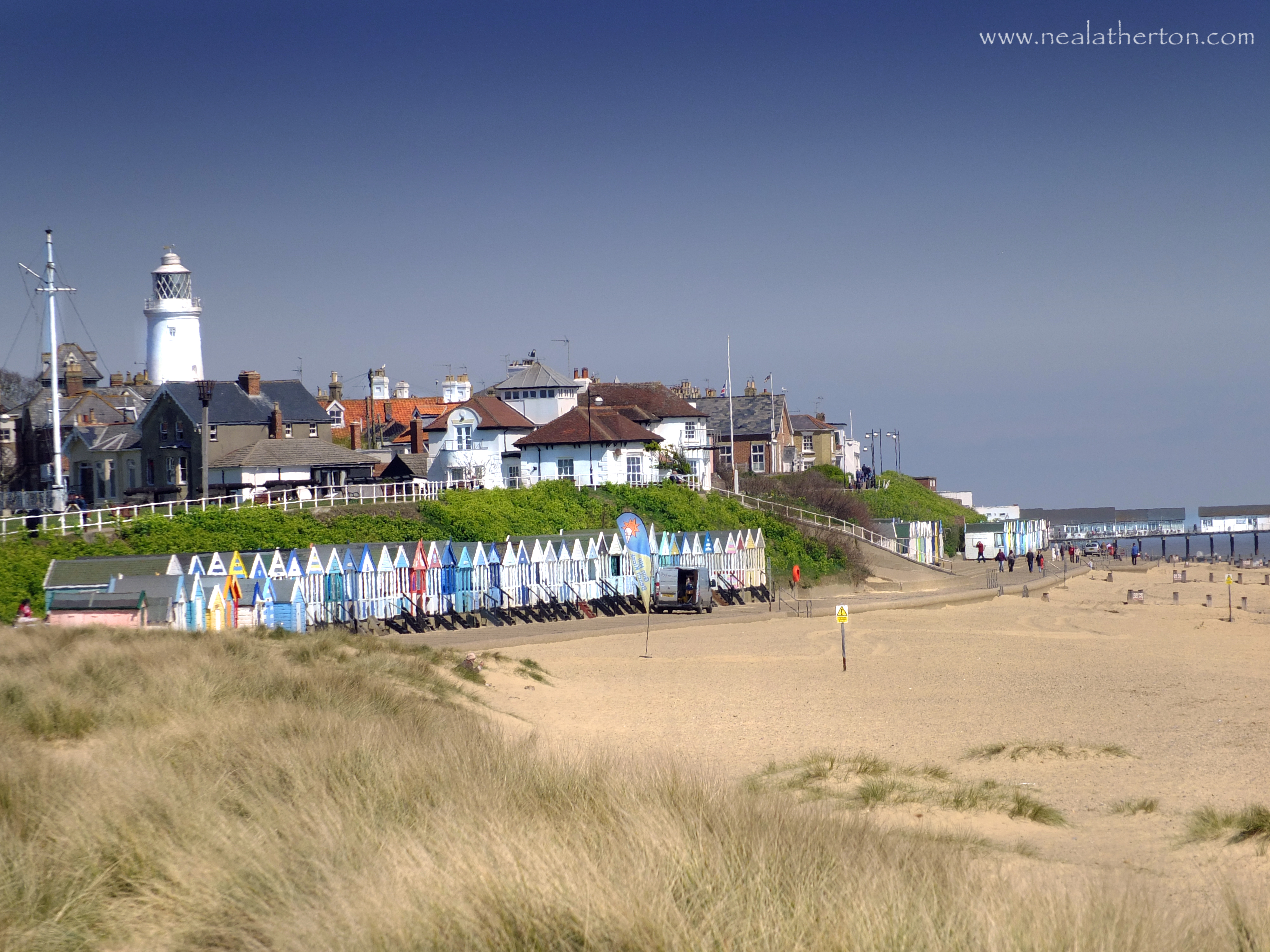 beach huts on sandy beach with houses and lighthouse