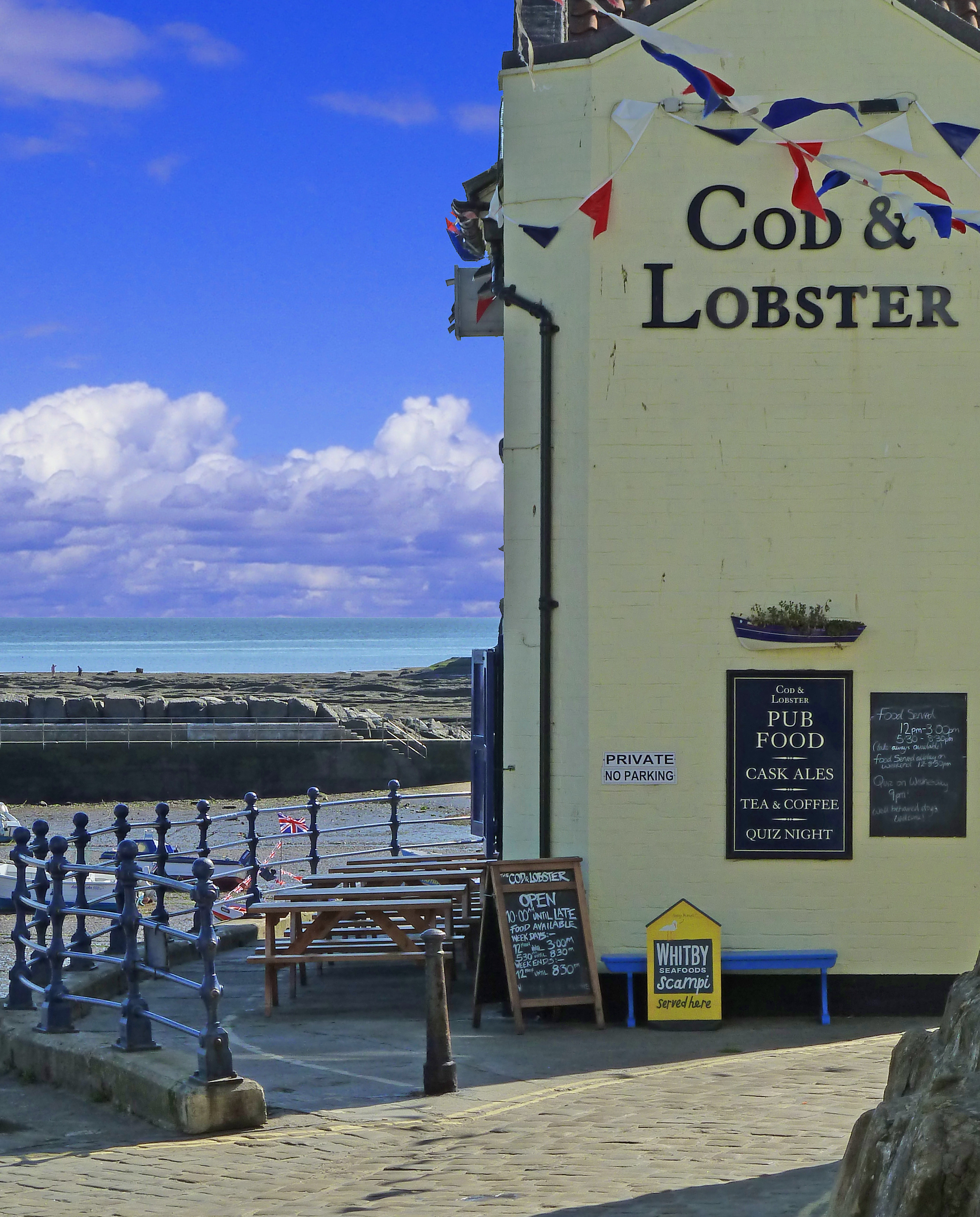 pub with signs and metal railings on harbour quayside with blue sky and clouds