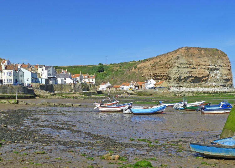 boats in harbour at low tide with cliffs and cottages on quayside