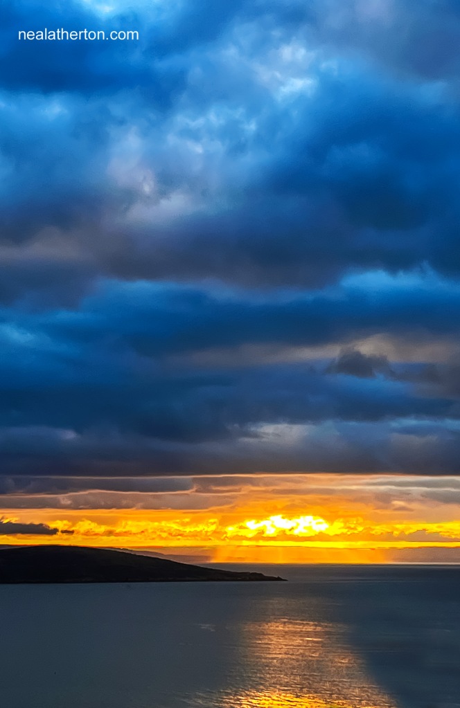Dark blue clouds hang over a golden sunset over Weston Super Mare Bay with light reflecting on the sea