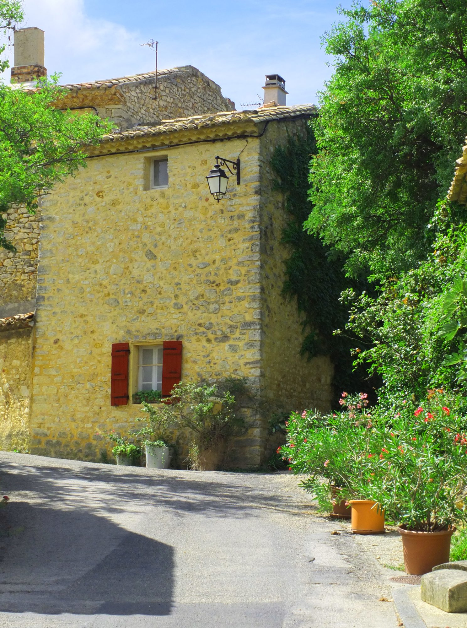 stone house with red shutters and tiled roof with trees and shrubs
