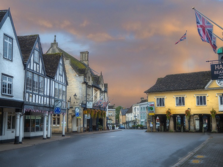Tudor stone buildings in old market square with road and flags under dark sky