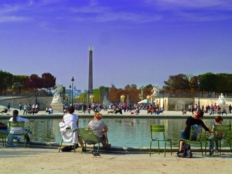 people sit round lake in gardens in city with ducks and egyptian monument