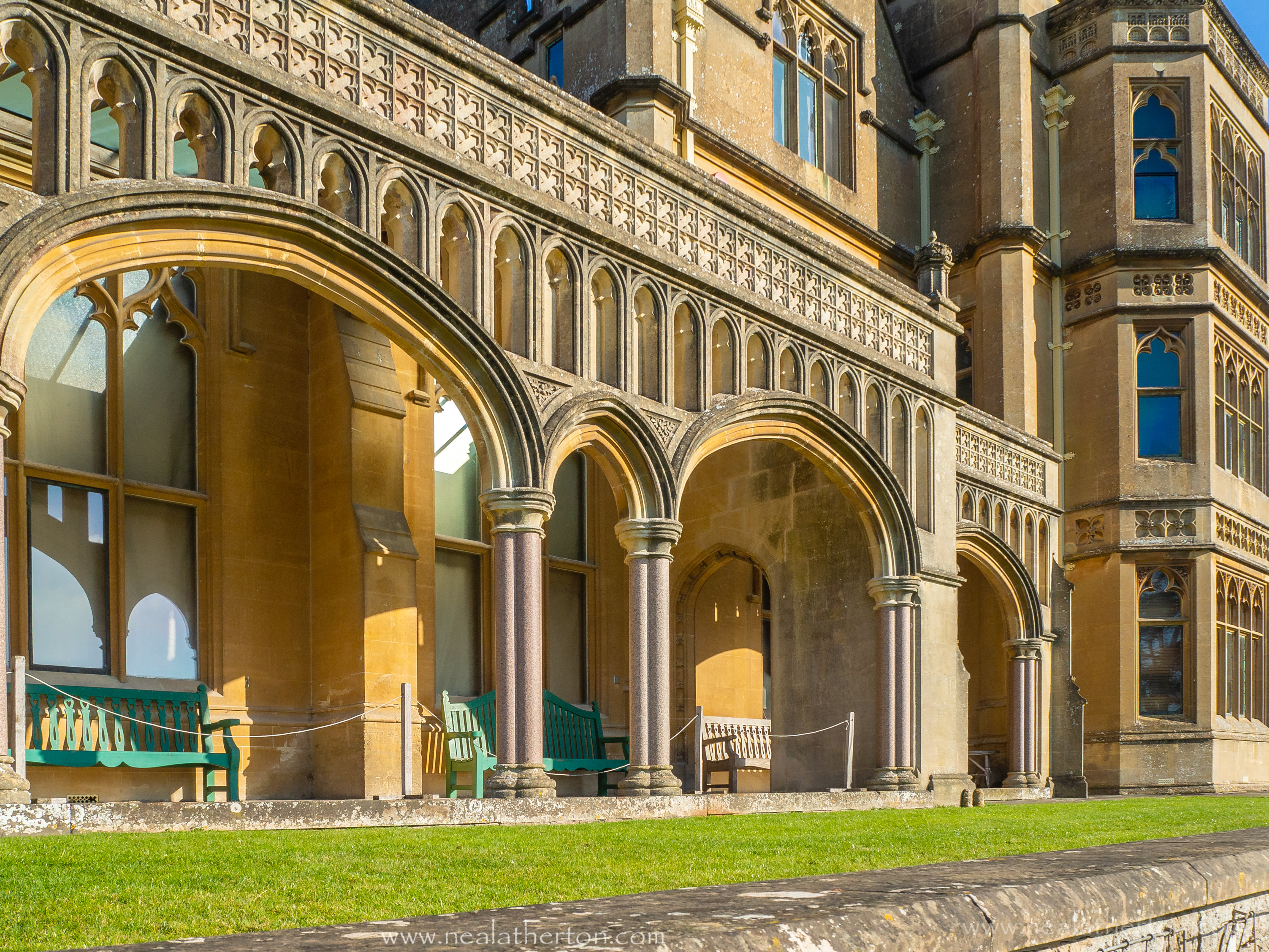 wooden seats in porch unser stone arch of large stone building with lawn