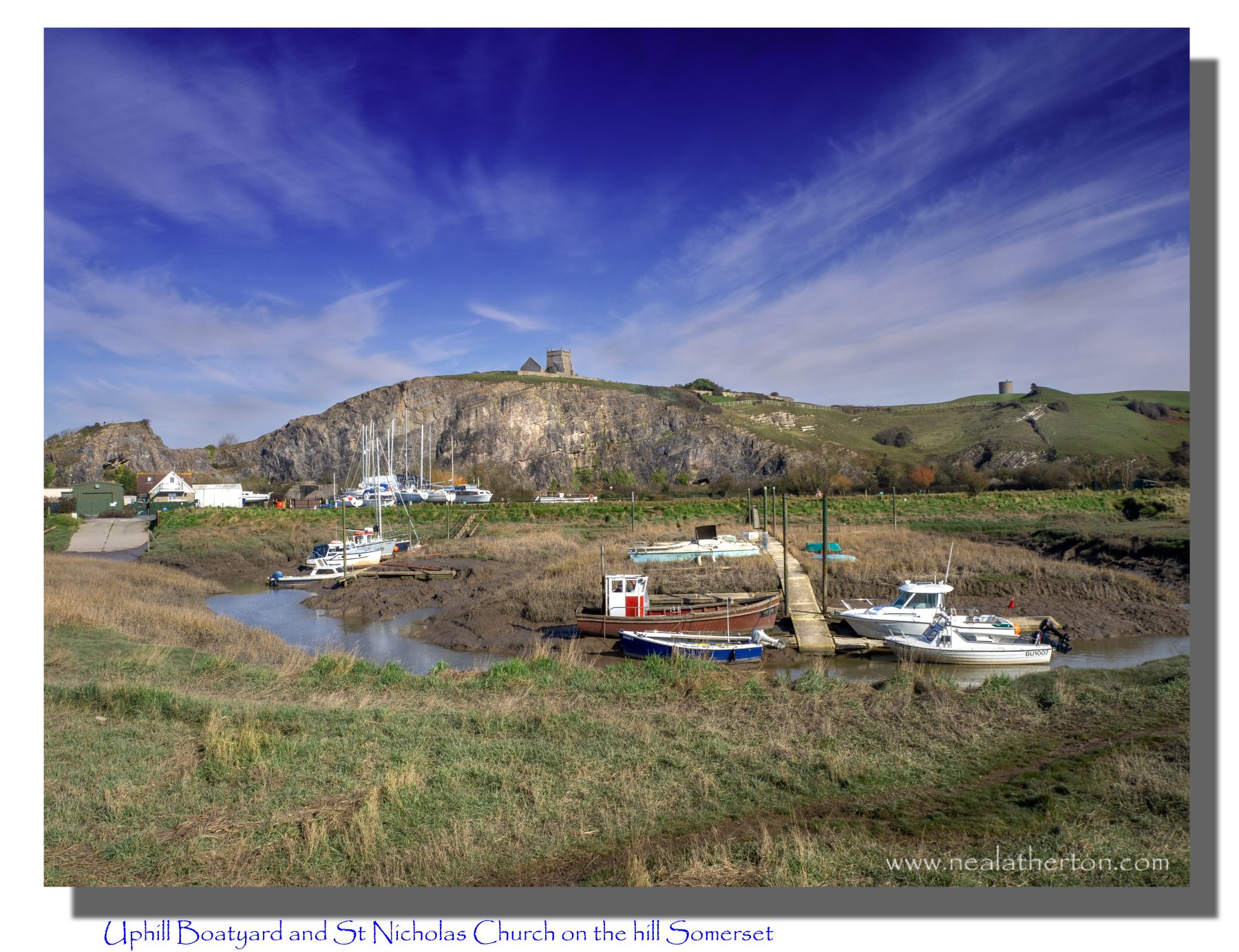 boats in river by boatyard with cliffs and church