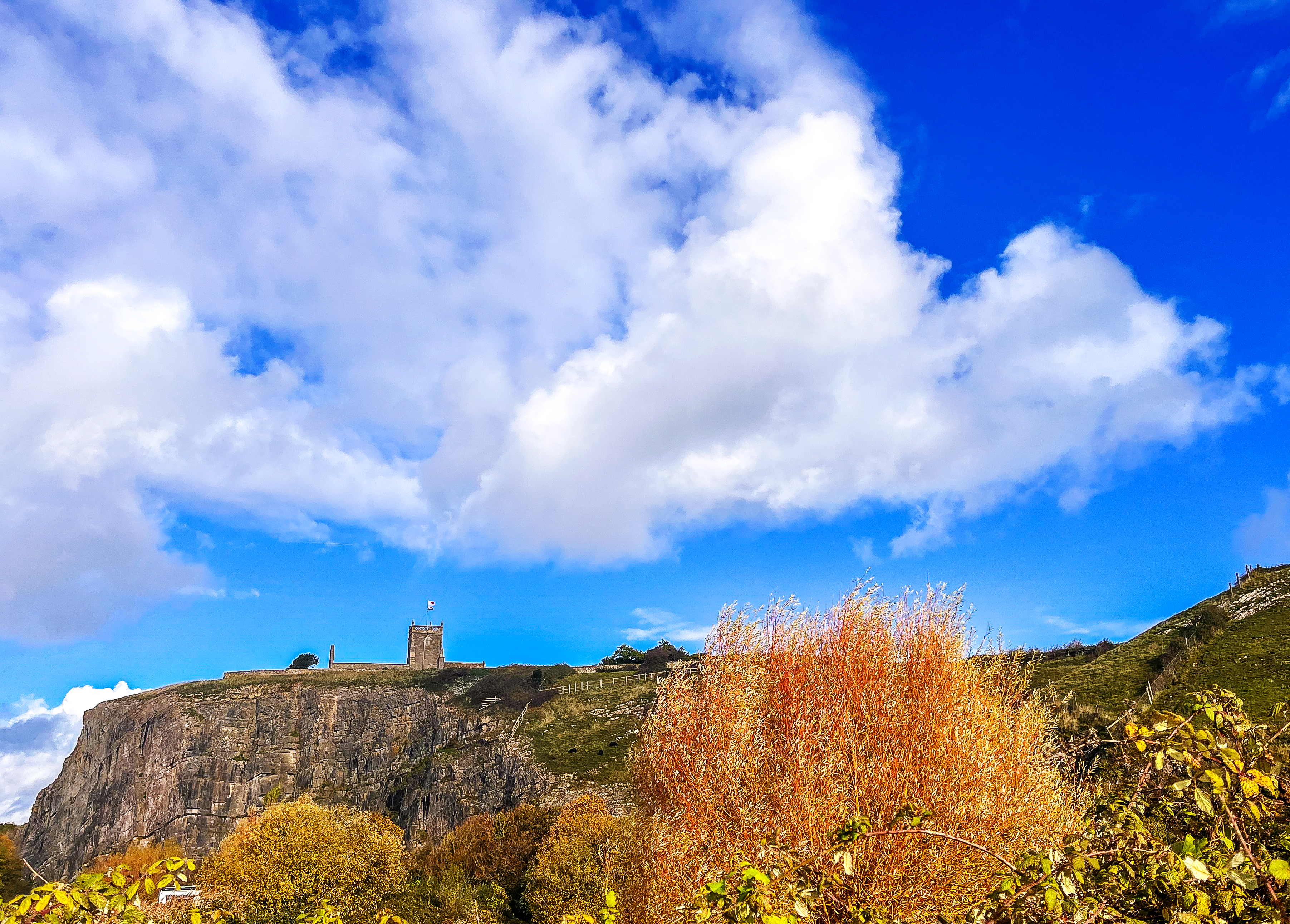 autumn colour tree and quarry with chuch on hill and blue cloudy sky