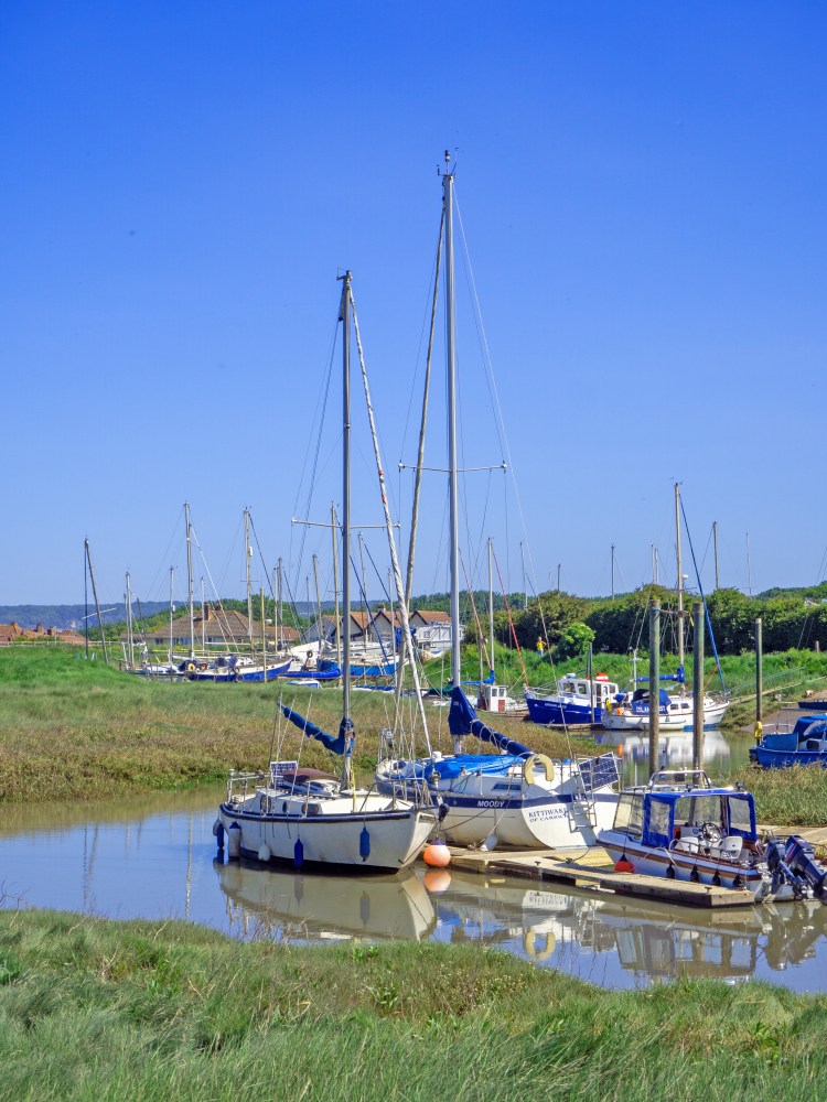 tachts on river near boatyard at high tide with grassy bank and blue sky