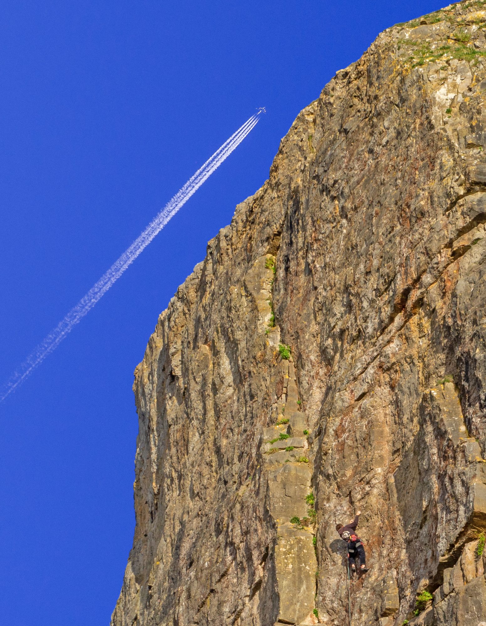 jet plane with contrail and climber on cliff side with deep blue sky