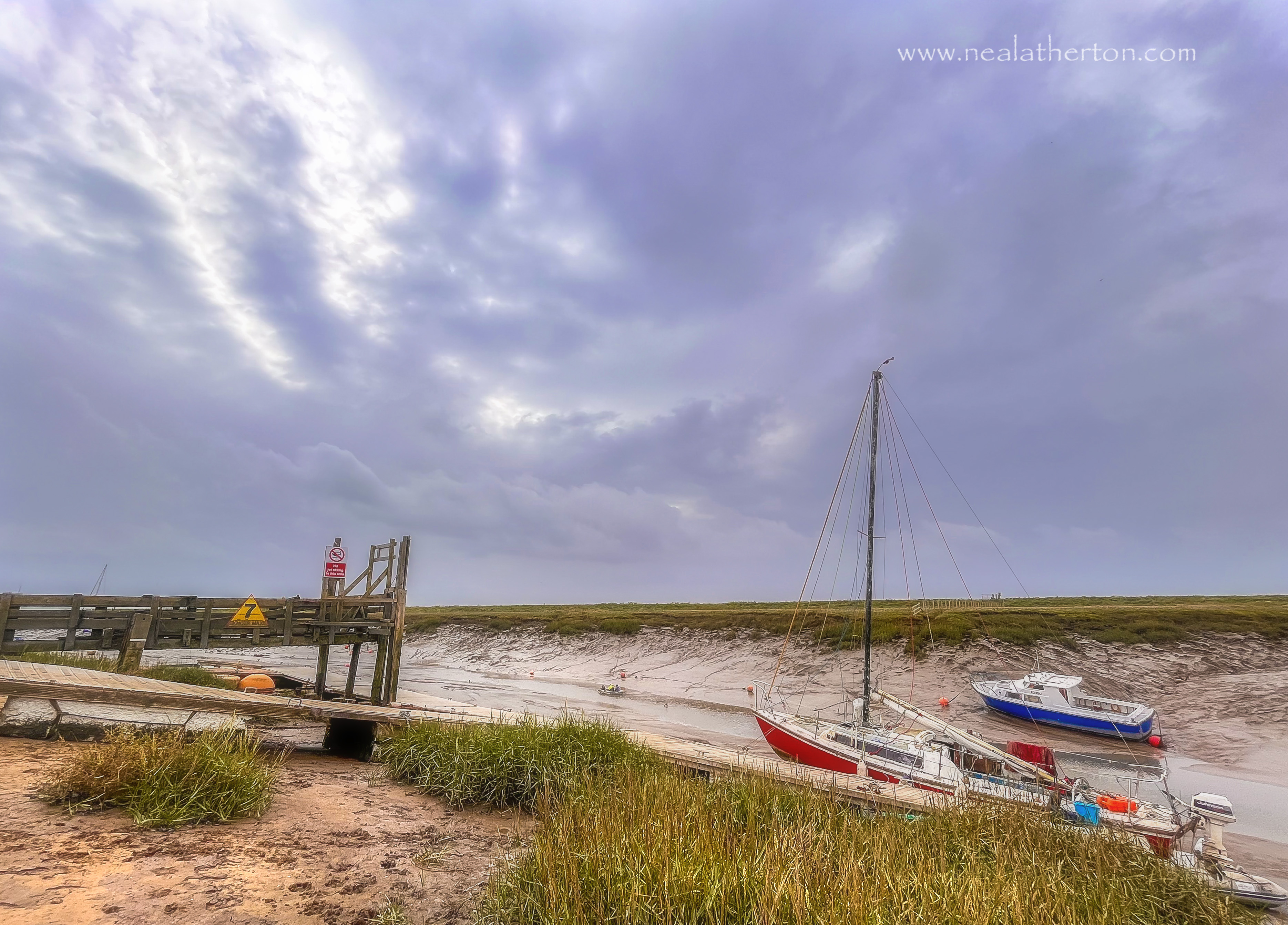 Yacht and boat at low tide in silt with wooden jetty and cols winter blue sky cloudy