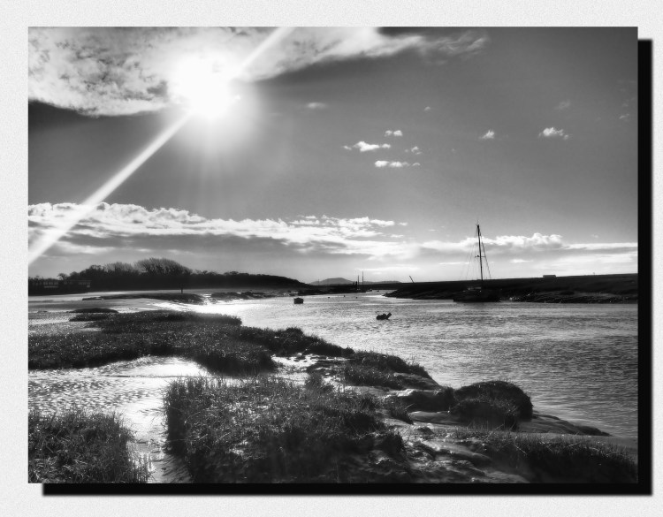 yacht and boats in black and white on river at high tide and sun breaking through clouds