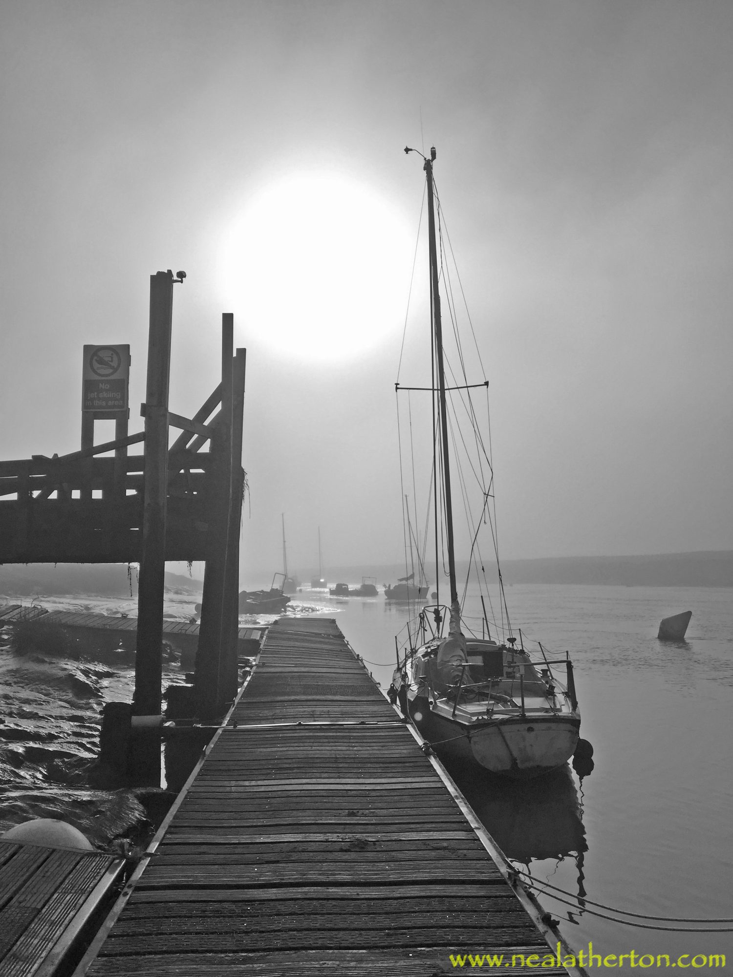 Yacht by river and wooden jetty with sun through heavy mist