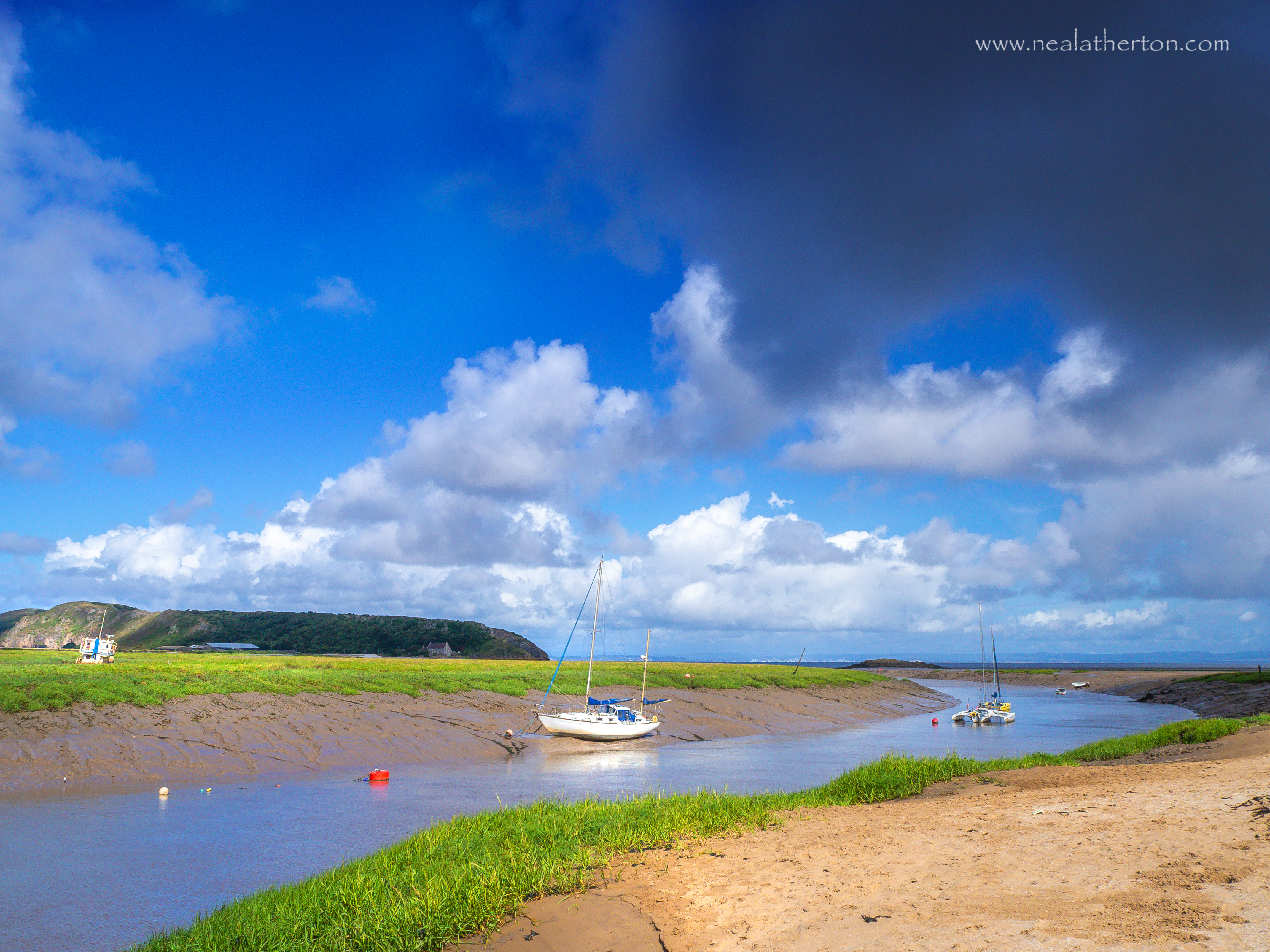 yachts moored on river with island in distance over green fields with blue squally sky