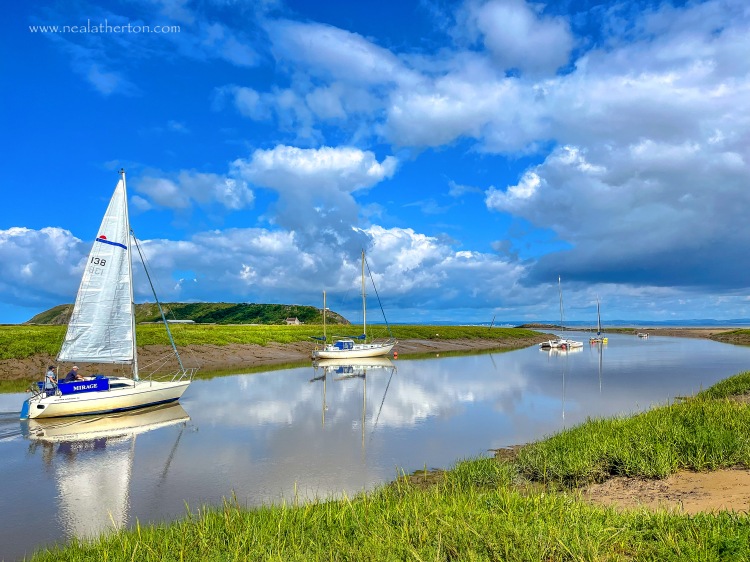 two yachts and boats on calm estuary on summers day with blue cloudy sky