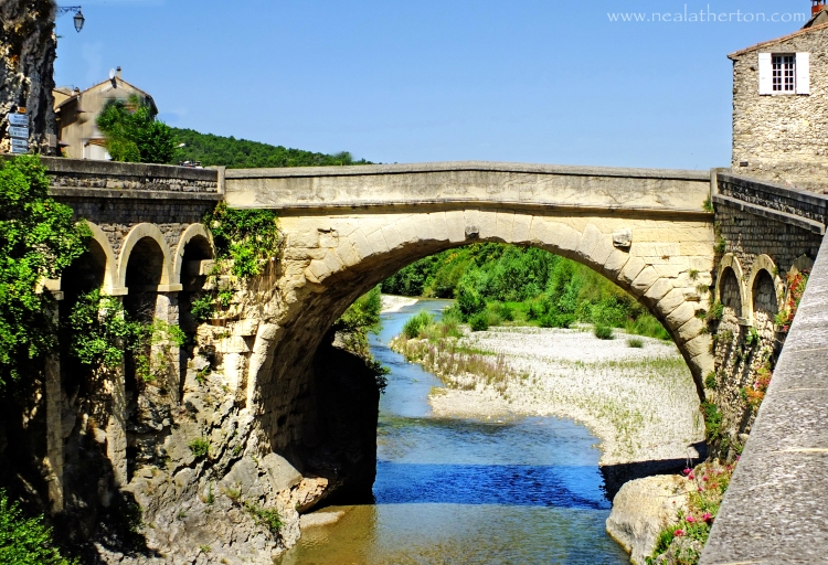 old stone Roman bridge over river by high wall