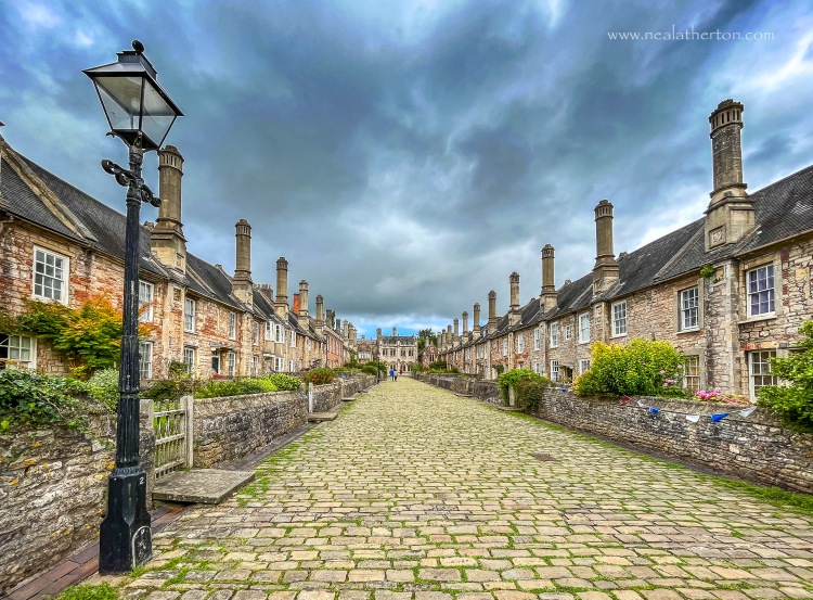 lamppost on cobbled street with ancient houses either side and an unsettled sky