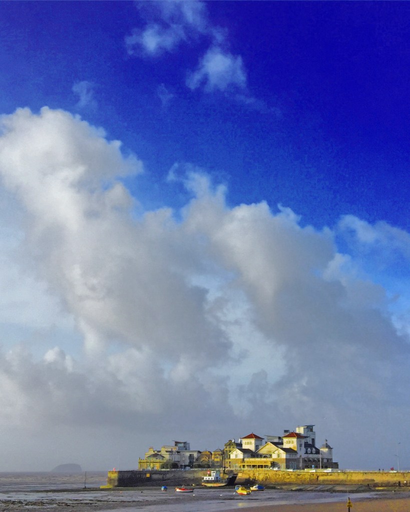 Island with buildings by sea with boats in water and large clouds in blue sky