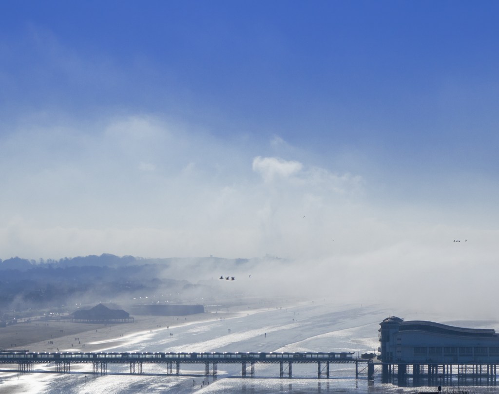 Long pier in sea with mist and birds flying over beach
