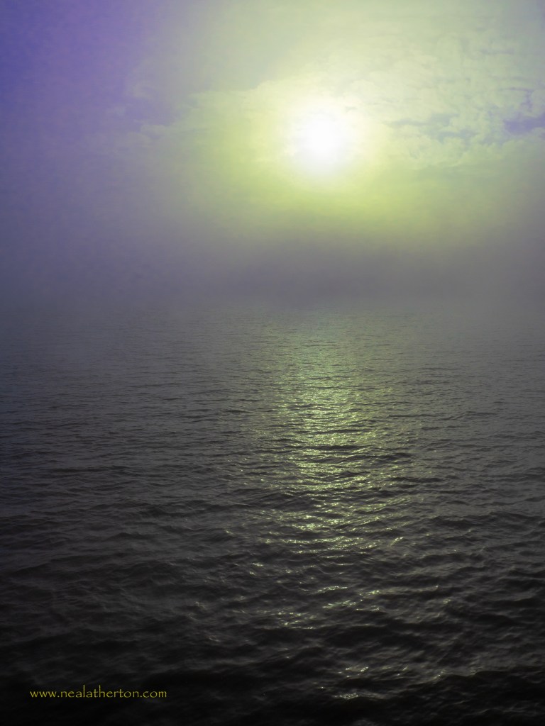 sun behing mist and clouds over calm sea