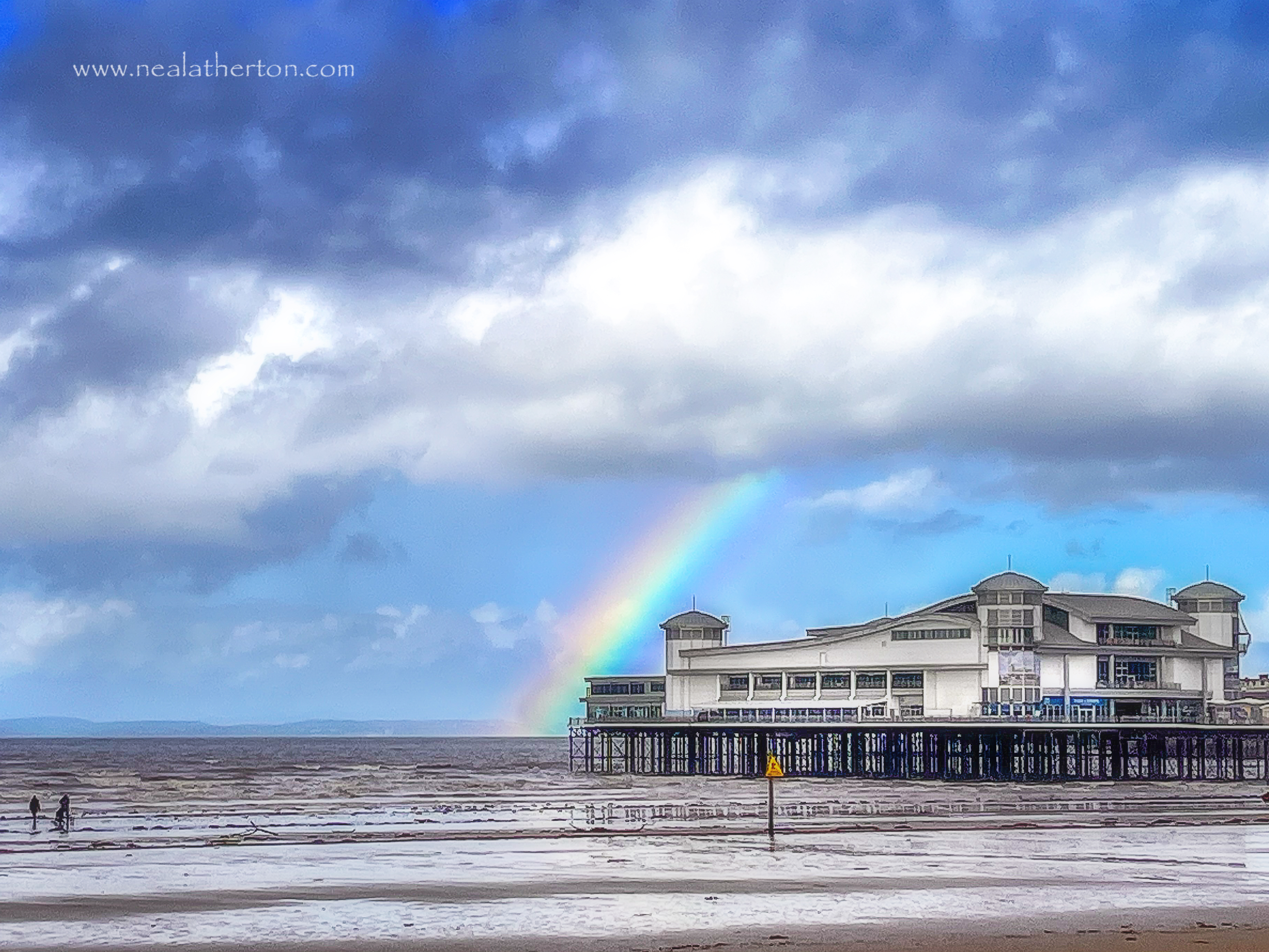 cold windy beach with two people by seashore with grand pier infront of stunning rainbow