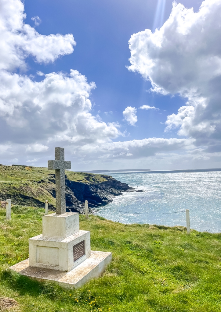 a cross on top of a monument on cliffs looking along the coast and out to sea under a showery sky