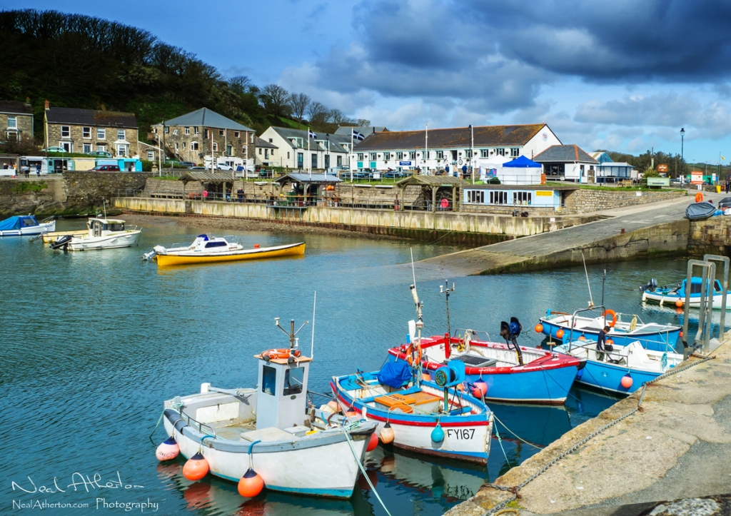 row of small fishing boats in a harbour at high tide with a slipway and building along the harbour edge